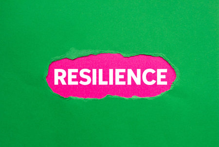 Resilience message written on ripped torn green paper on pink background. Conceptual resilience...