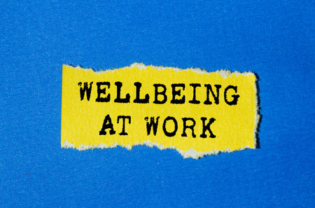 Wellbeing at work message written on ripped torn yellow paper on blue background. Conceptual wellbeing at work symbol. Copy space.の写真素材