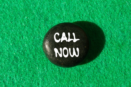 Call now message written on black stone on green background. Conceptual call now symbol. Copy space.