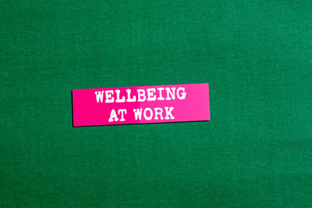 Wellbeing at work message written on pink paper sticker on green background. Conceptual wellbeing at work symbol. Copy space.の写真素材