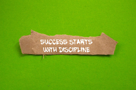 Success starts with discipline message written on torn brown paper piece on green background....