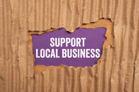 Support local business message written on ripped torn cardboard paper on purple background. Conceptual support local business symbol. Copy space.の写真素材