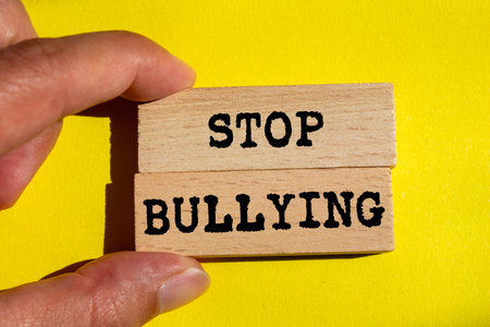Stop bullying message written on wooden blocks on yellow background. Conceptual stop bullying...