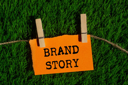 Brand story message written on torn torn orange paper piece on green grass background. Conceptual brand story symbol. Copy space.の写真素材