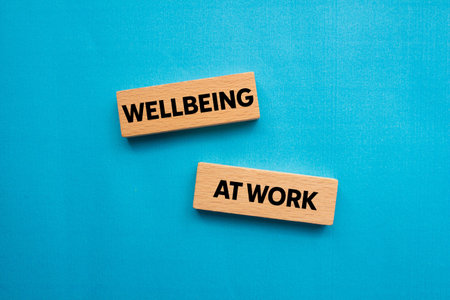 Wellbeing at work message written on wooden blocks on blue background. Conceptual wellbeing at work...