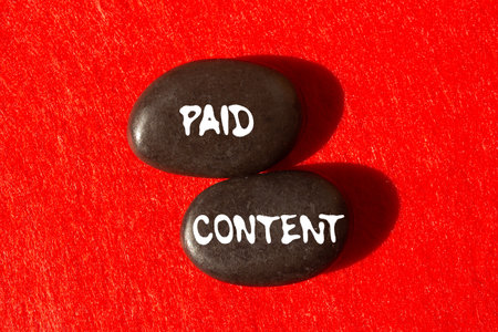 Paid content message written on black stones on red background. Conceptual paid content symbol. Copy space.の写真素材