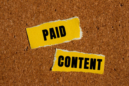 Paid content message written on ripped yellow paper pieces on brown background. Conceptual paid content symbol. Copy space.の写真素材
