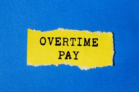 Overtime pay message written on torn yellow paper on blue background. Conceptual overtime pay symbol. Copy space.の写真素材