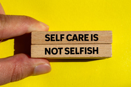 Self care is not selfish message written on wooden blocks on yellow background. Conceptual self care is not selfish symbol. Copy space.の写真素材