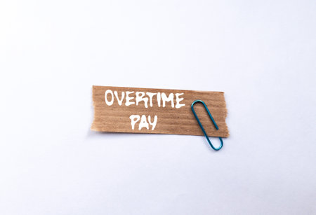 Overtime pay message written on ripped torn brown paper piece on white background. Conceptual overtime pay symbol. Copy space.の写真素材