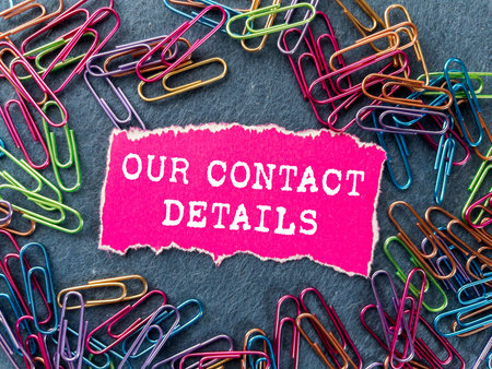 Our contact details message written on ripped torn pink paper piece on gray background. Conceptual...