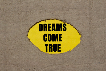 Dreams come true message written on torn torn cardboard paper on yellow background. Conceptual dreams come true symbol. Copy space.の写真素材