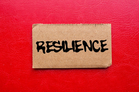 Resilience message written on torn torn cardboard paper piece on red background. Conceptual...