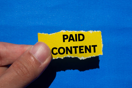 Paid content message written on ripped torn yellow paper piece on blue background. Conceptual paid content symbol. Copy space.の写真素材
