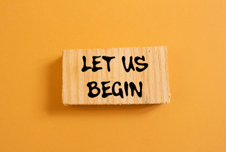 Let us begin message written on wood piece on orange background. Conceptual let us begin symbol. Copy space.の写真素材