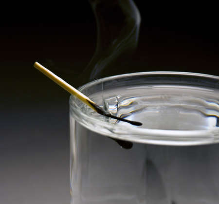 A match stick just put out in a glass of waterの写真素材