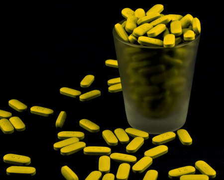 Yellow pills spilling out of a shot glassの写真素材