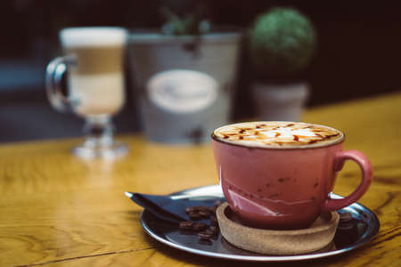 Hot cappuccino with caramel decoration on foamy surface. On metal plate with coffee beans. With some decoration on the background on wooden table.の写真素材