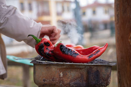 Hand checking red chili peppers grilling on BBQの写真素材