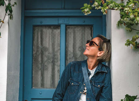 Pretty fashionable woman standing in doorway of old house. Cool dressed lady in front of turquoise...