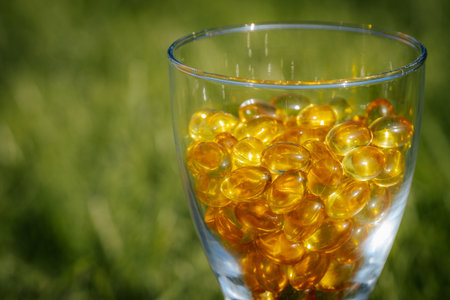 Cod liver oil omega 3 gel capsules in a glass on green grassの写真素材