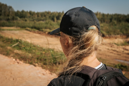 A girl in a cap with a backpack on a country road.の写真素材