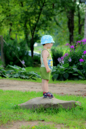 Little boy standing on a stone in the park and looking at the cameraの写真素材