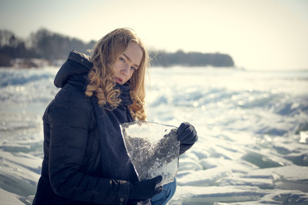 Beautiful young woman with ice skates on frozen lake in winterの写真素材