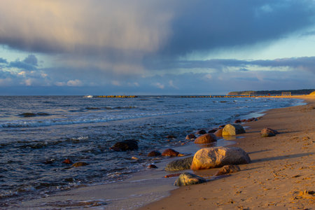 Baltic sea coast at sunset. Dramatic sky, glowing clouds, waves and water splashes. Latviaの写真素材