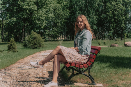 beautiful young woman sitting on bench in park and looking at cameraの写真素材