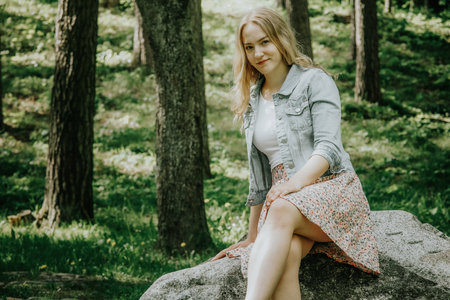 Portrait of a beautiful young woman sitting on a rock in the forestの写真素材