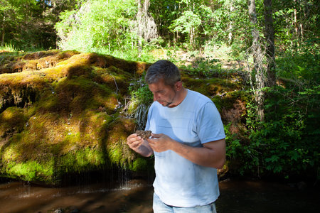 Mature man drinking water from a small waterfall in a forest streamの写真素材