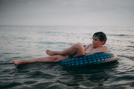 A young boy is lying on an inflatable ring in the sea.の写真素材