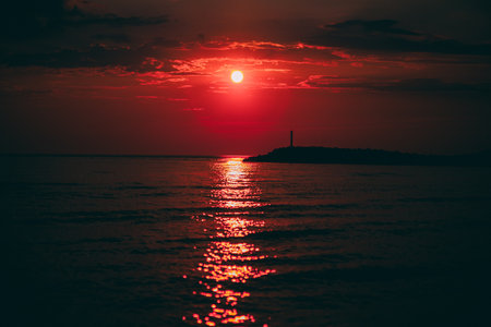 Beautiful red sunset over the sea with a lighthouse in the backgroundの写真素材