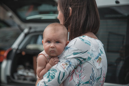 Mother holding her baby in her arms while standing in front of the carの写真素材