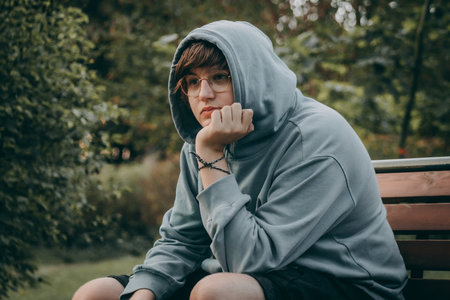 Portrait of a young man in a hood on a park benchの写真素材