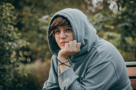 Portrait of a man in a hoodie on a park benchの写真素材