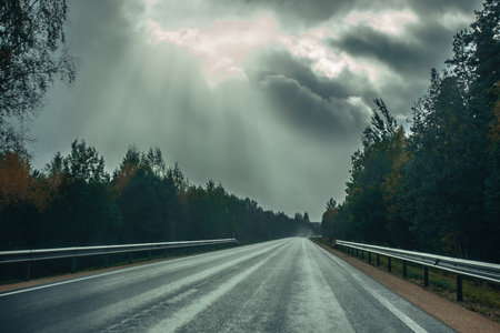 Autumn landscape with asphalt road through the forest and cloudy sky.の写真素材