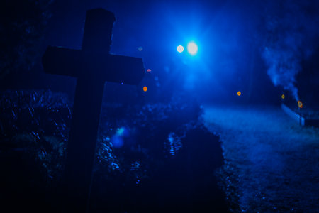 Cross at cemetery at night with fog and lights. Horror Halloween concept. Selective focusの写真素材