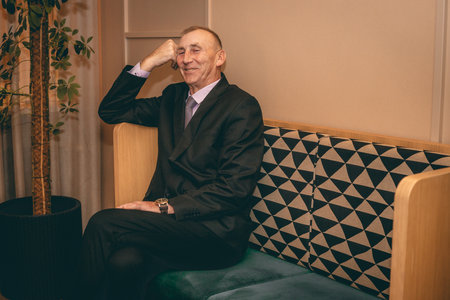 Elderly man in a suit sits on a chair in a cafe.の写真素材