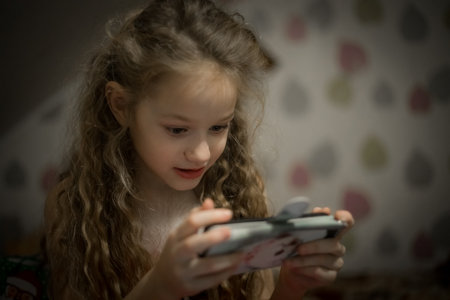 Little girl playing games on a mobile phone at home. The child uses a smartphone.の写真素材