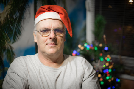 Portrait of a senior man in a Santa Claus hat on the background of the Christmas tree.の写真素材
