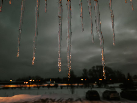 Icicles hanging from the roof of a house in the eveningの写真素材