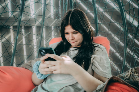 Young woman sitting in a hammock and using a mobile phone.の写真素材