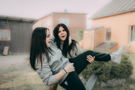 Two beautiful young women in a gray sweatshirt and jeans are having fun on the streetの写真素材
