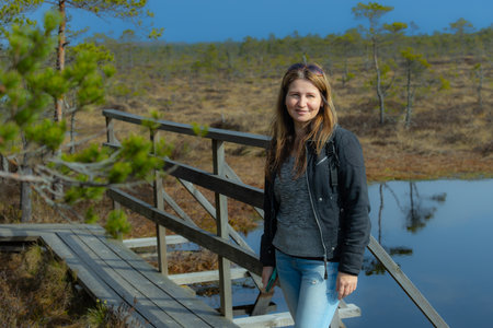 Portrait of a young woman standing on a wooden bridge over a swampの写真素材