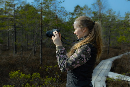 Young woman with a camera in a pine forest. The girl looks at the camera.の写真素材