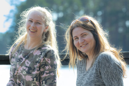 Two smiling women on a bench in the park in the sun.の写真素材