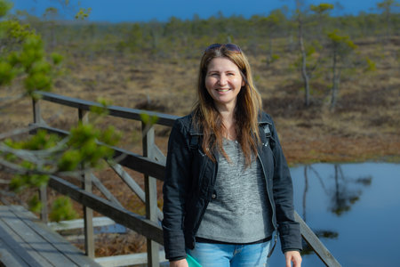 Portrait of a smiling young woman standing on wooden bridge in swampの写真素材