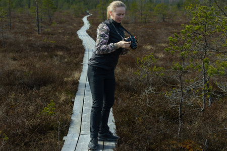 Young woman on a trail in the bog with a camera in her handsの写真素材